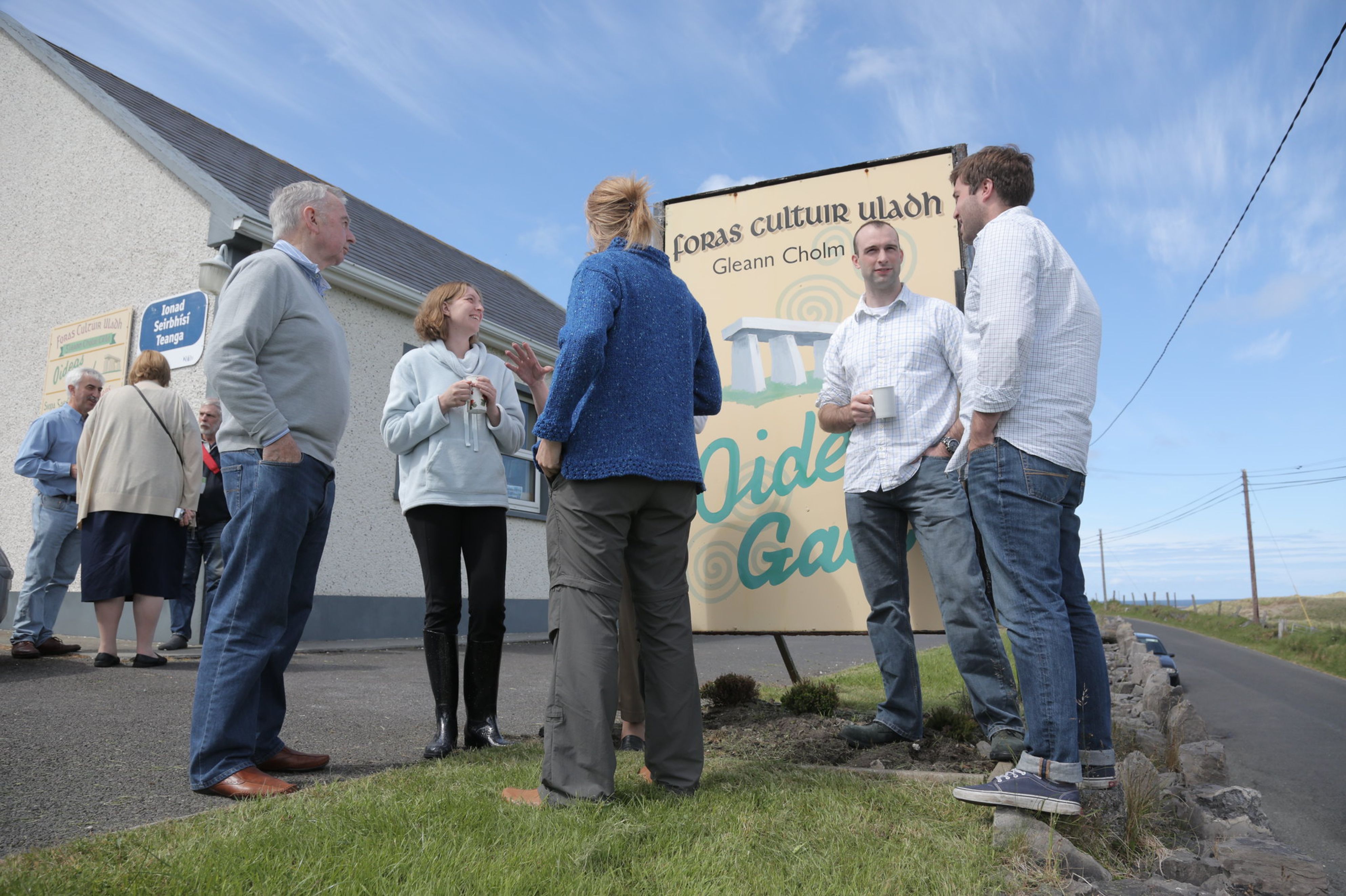 People talking and drinking tea at the Oideas Gael sign during an Irish language course