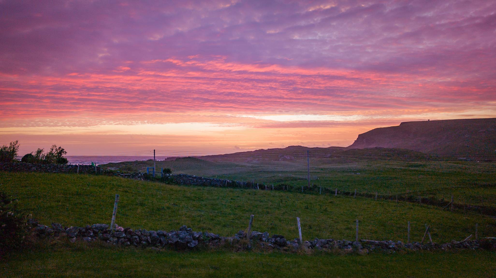 Luí na gréine os cionn na Dumcha, Gleann Cholm Cille, agus dathanna idir bhuí, bhándearg agus dúghorm sa spéir